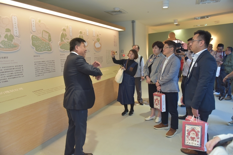 導覽員於臺灣客家茶文化館展廳中向訪客介紹茶葉製程與香氣發酵流程，觀眾專注聆聽，現場充滿文化與學習氛圍，呈現深度導覽與茶文化教育特色。