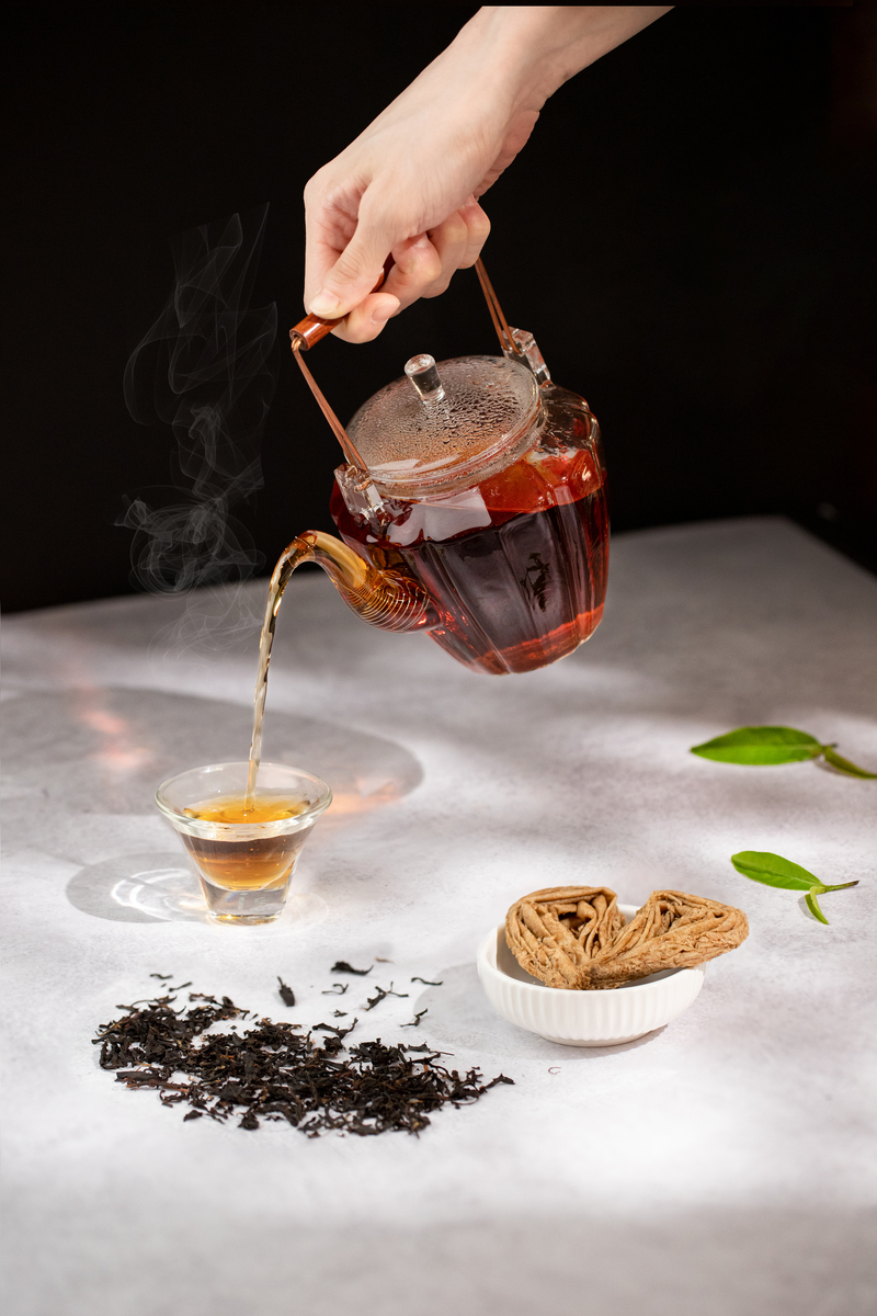手沖台灣紅茶示意圖，玻璃茶壺中溫熱紅茶正倒入透明茶杯，茶桌上擺有乾燥茶葉、水滴蛋捲與紅茶葉，營造溫潤茶香與職人美感氛圍
