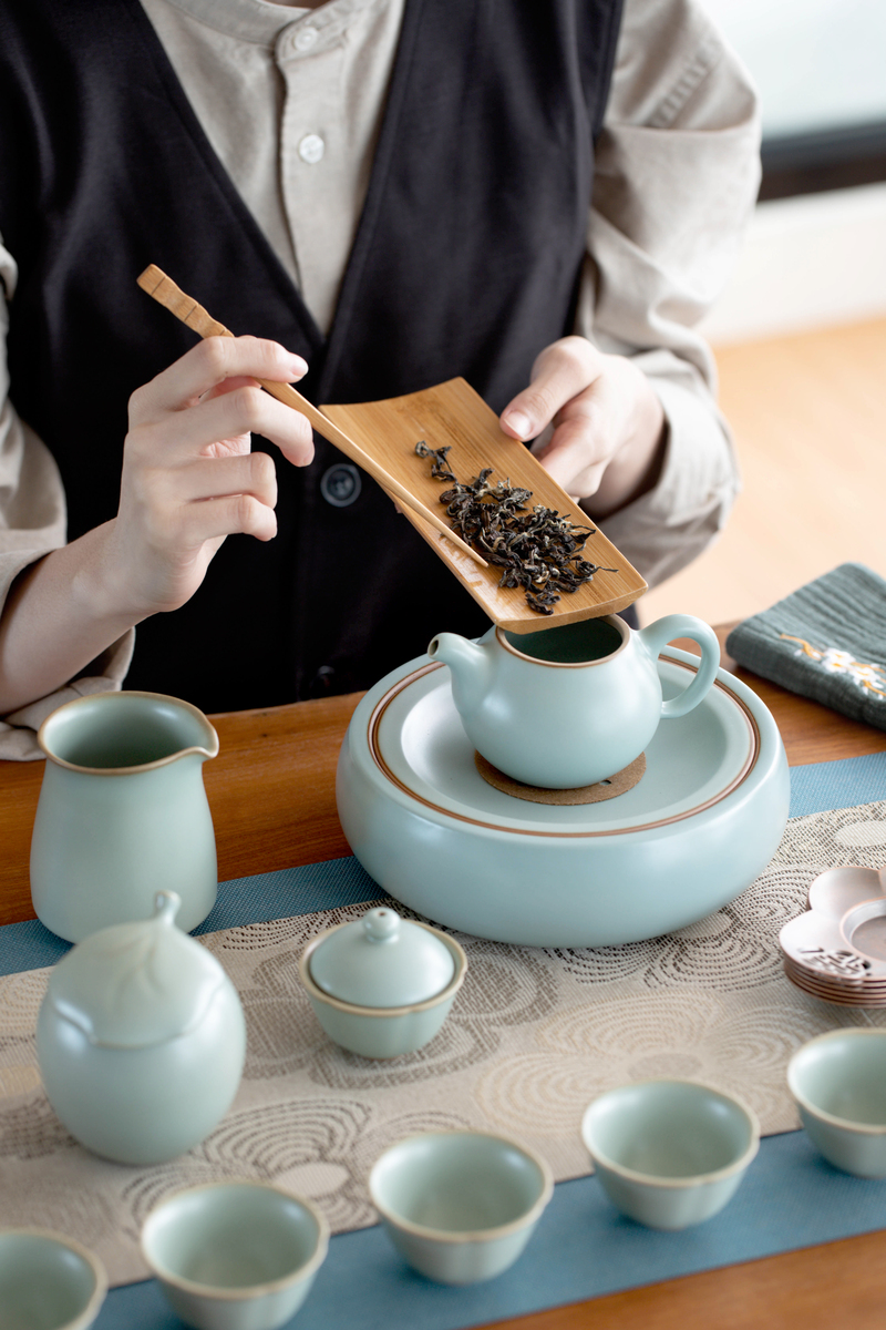 台灣茶室茶席擺設，示範茶師正以竹製茶則將茶葉投入青瓷壺中，搭配傳統功夫茶具與茶道布巾，展現台灣烏龍茶沖泡儀式，場景位於福爾摩沙茶館
